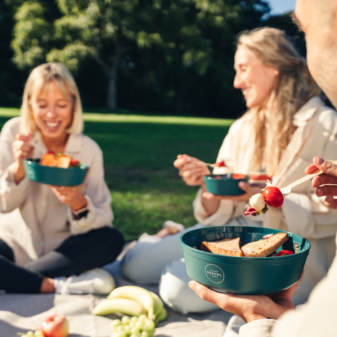 Personen sitzen zusammen im Park beim Picknick und essen aus Rebowl Geschirr